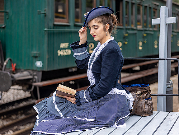 Junge Dame im zeitgenössischen lila schwarzen Kleid mit Mantel und Hut aus den 1910er Jahren