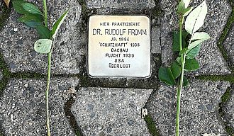 Ein Stolperstein neben dem zwei weiße Rosen zum Gedenken abgelegt wurden.
