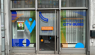 Eingang eines Ladenlokals mit mit Logos bunt beklebter Fenster-Front.