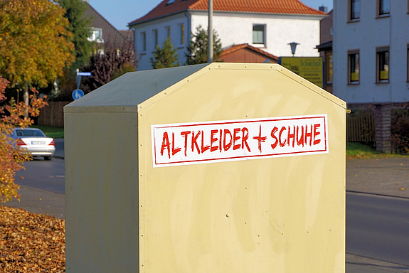 Ein hellbeigefarbener Container mit derm Aufdruck Altkleider plus Schuhe